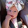 baby, child, car_seat, safety_harness, blue_eyes, floral_bow, pink_clothing, infant, chewing_fist, sunlight, shadow, seatbelt, closeup, portrait, cute, indoor, expression, headwear, person, car_interior