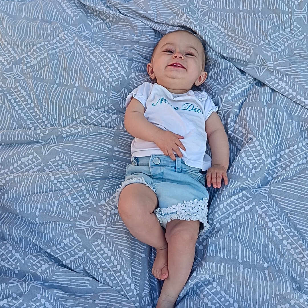 Emya a rejoint le concours — aidez-le/la à gagner de superbes lots ! baby, blanket, casual_clothing, child, cute, denim_shorts, grass, happy, infant, lying_down, outdoor, patterned, person, playful, portrait, relaxed, smiling, summer, white_shirt, young_child