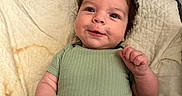 Michael is registered to the contest to win money with this photo: baby, infant, child, smile, quilt, blanket, onesie, green_clothing, curly_hair, lying_down, cute, indoor, soft_texture, bed, happy, face, skin, person, young_child, cozy
