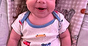 Michael is registered to the contest to win money with this photo: baby, blanket, child, clothing, comfort, cute, expression, face, hand, happy, indoors, infant, onesie, pattern, person, portrait, sitting, skin, smiling, young