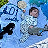 baby, infant, blanket, grass, plush_toys, sea_creatures, wooden_sign, hello_world, outdoor, one_month, clothing, lying_down, cute, child, nature, soft_toys, blue, white, green, portrait