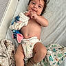 baby, blanket, child, cute, diaper, fabric, face, footwear, hand, happy, indoor, infant, lying_down, patterned_blanket, playpen, plush_toy, skin, smile, sock, soft_texture