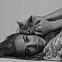 animal, black_and_white, calm, cat, close_up, expression, face, fur, hair, hands, indoor, intimate, looking_at_camera, lying_down, monochrome, pet, portrait, soft_lighting, texture, woman