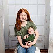 Ariel joined the competition — help win amazing prizes! child, baby, red_hair, green_shirt, blue_jeans, smiling, sleeping, baby_wrap, sitting, indoor, window, stool, headband, peaceful, portrait, siblings, happy, family, casual_clothing, wooden_floor
