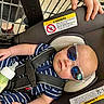baby, sunglasses, car_seat, shopping_cart, baby_bottle, hand, striped_clothing, infant, child, seat_belt, safety, retail, shopping, toddler, cute, protective_hand, blue_clothing, reflection, casual, portrait