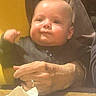 Carter is registered to the contest to win money with this photo: baby, child, infant, face, hands, adult, holding, yellow_clothing, gray_clothing, table, napkin, indoor, portrait, expression, cute, skin, person, closeup, seated, cozy