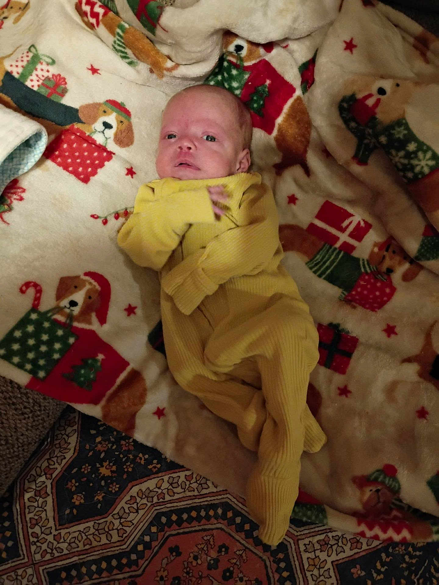 Carter joined the competition — help win amazing prizes! baby, infant, yellow_onesie, blanket, holiday_theme, dog_pattern, gifts, carpet, floor, lying_down, indoor, cute, small, child, person, warm, soft_texture, festive, cozy, curious