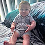 Mavrick is registered to the contest to win money with this photo: baby, child, infant, romper, striped_clothing, couch, blanket, indoor, curtain, vertical_blinds, feet, hands, face, expression, sitting, cozy, daylight, home, cute, curious