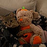 tabby_cat, plush_toy, teddy_bear, pumpkin_costume, blanket, couch, indoor, cozy, pet, animal, feline, soft_toy, snuggling, comfort, relaxation, home, furniture, fabric, cute, autumn