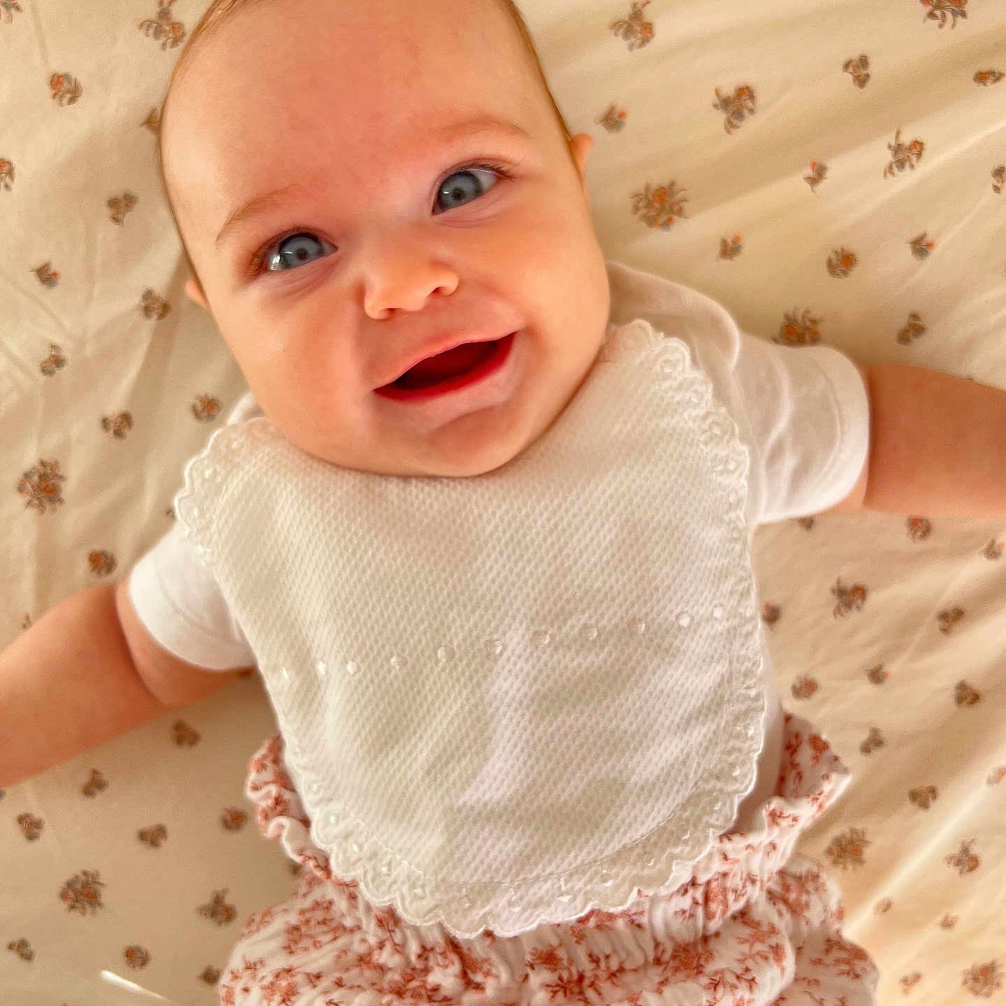 Mily-Rose participe au concours pour gagner de l'argent avec cette photo : arms, baby, baby_girl, blue_eyes, child, clothing, cute, face, floral_bloomers, floral_sheet, happy, head, indoors, infant, lying_down, portrait, skin, smiling, soft_light, white_bib