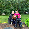 Solomon Douglas is registered to the contest to win money with this photo: dog, people, friends, smiling, outdoor, garden, backyard, trees, grass, wheelchair, pet, curly_fur, brown_dog, portrait, posing, joyful, woman, sunglasses, plants, daylight