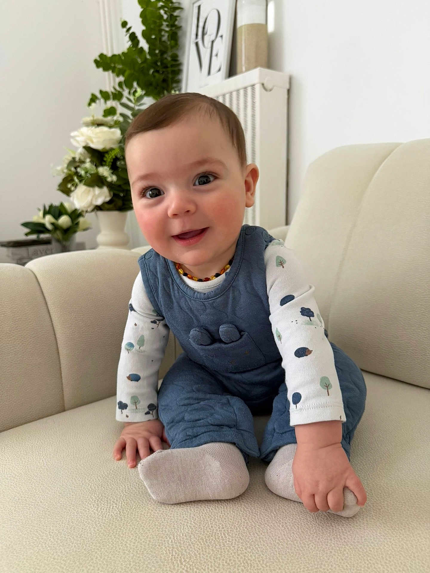 Hamza participe au concours pour gagner de l'argent avec cette photo : baby, infant, child, couch, sofa, sitting, smile, happy, cheeks, eyes, romper, socks, hand, toe, indoor, plant, vase, decor, portrait, face