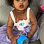 toddler, child, curly_hair, sippy_cup, purple_skirt, crocheted_top, couch, leather, seated, wide_eyes, expression, indoor, hands, clothing, baby, cute, portrait, skin, furniture, young_child