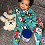 baby, child, smiling, pajamas, mickey_mouse, couch, teddy_bear, toy, furniture, indoor, person, face, happy, curly_hair, jar, container, footed_pajamas, relaxing, cute, cozy