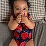 baby, infant, smiling, headband, strawberry_pattern, onesie, lying_down, bed, pillow, happy, cute, child, skin, hand, face, person, indoors, young, playful, bracelet