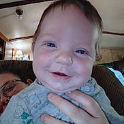 Ryder joined the competition — help win amazing prizes! baby, smile, blue_eyes, hand, adult, indoor, ceiling, lamp, glasses, person, clothing, couch, wood, home, portrait, happy, face, child, holding, cozy