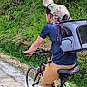 man, bicycle, cat, pet, outdoor, forest, greenery, cycling, path, nature, backpack, animal, harness, casual_clothing, sport, adventure, road, helmet_absent, daytime, travel