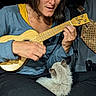 woman, cat, ukulele, music, indoor, playing, pet, lap, cozy, casual_clothing, long_hair, seated, furry, instrument, wood, black_pants, focused, relaxed, comfort, bond