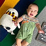 baby, infant, smile, plush_toy, owl, knitted_blanket, colorful, striped_clothing, dinosaur_print, green_romper, happy, lying_down, milestone_board, 6_months, cute, child, playful, indoor, soft_texture, joyful