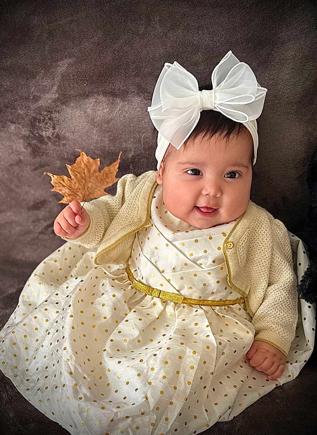 Keila is registered to the contest to win money with this photo: baby, bow, cardigan, child, clothing, cute, dress, face, hand, happy, headband, indoor, infant, leaf, person, polka_dots, portrait, sitting, smiling, warm