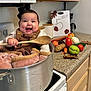 Keila joined the competition — help win amazing prizes! apple, baby, blanket, carrot, child, cooking_pot, countertop, green_bell_pepper, happy, infant, kitchen, milestone, onion, potato, sign, smiling, stove, tomato, vegetables, wooden_spoon