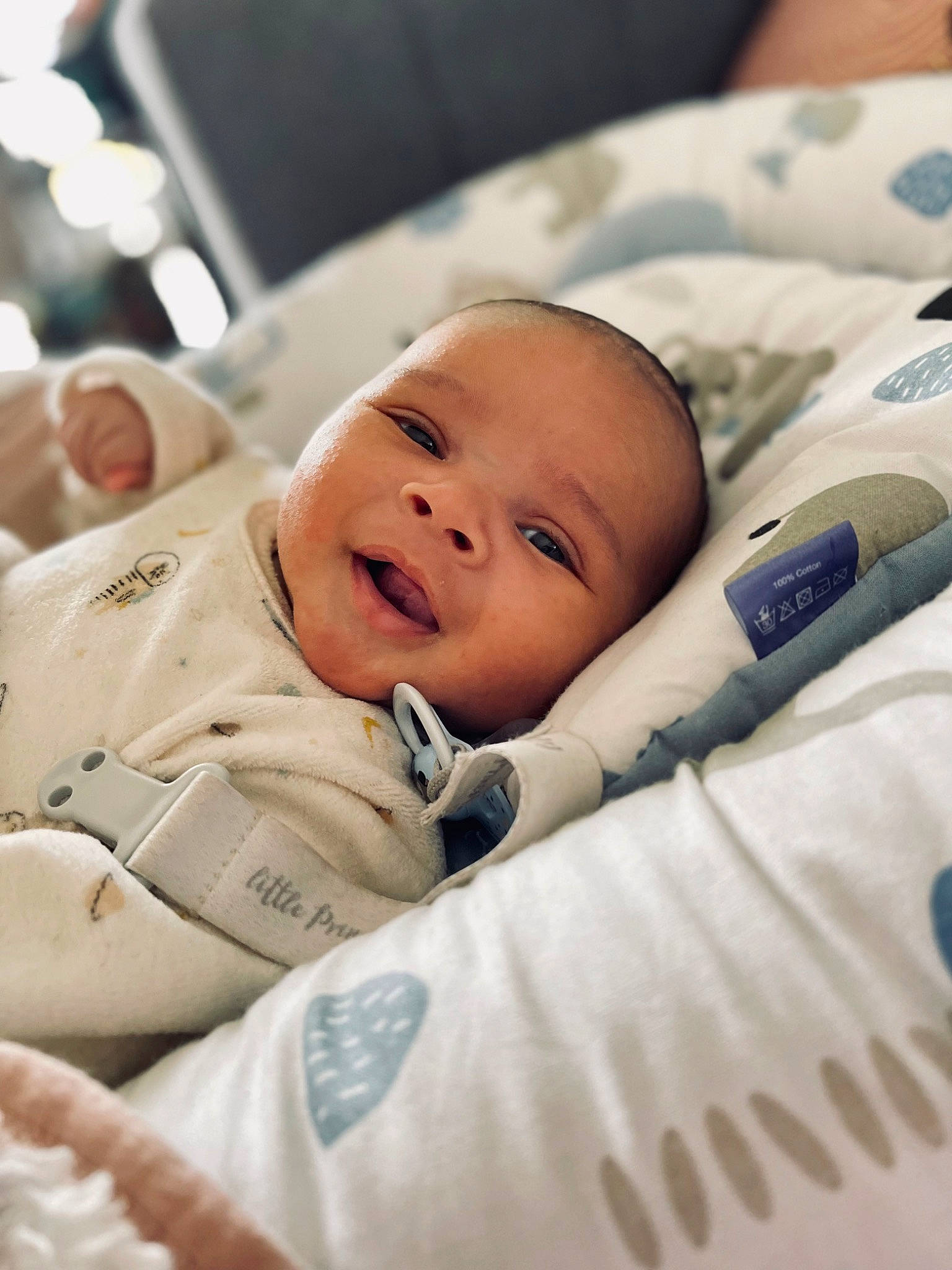 Sacha participe au concours pour gagner de l'argent avec cette photo : baby, baby_toddler_clothing, cheek, child, comfort, happy, linens, person, portrait_photography, product, room, sitting, skin, sleeve, smile, toddler