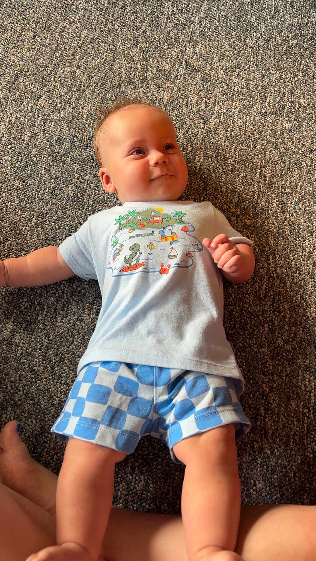 Garrett is registered to the contest to win money with this photo: baby, child, infant, tshirt, shorts, carpet, floor, smile, happy, cute, lying_down, clothing, pattern, blue, white, cartoon, person, skin, indoor, legs