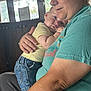 Garrett joined the competition — help win amazing prizes! baby, adult, holding, indoor, window, natural_light, clothing, person, affection, casual, denim_shorts, tshirt, skin, face, hand, comfort, expression, seated, closeup, family