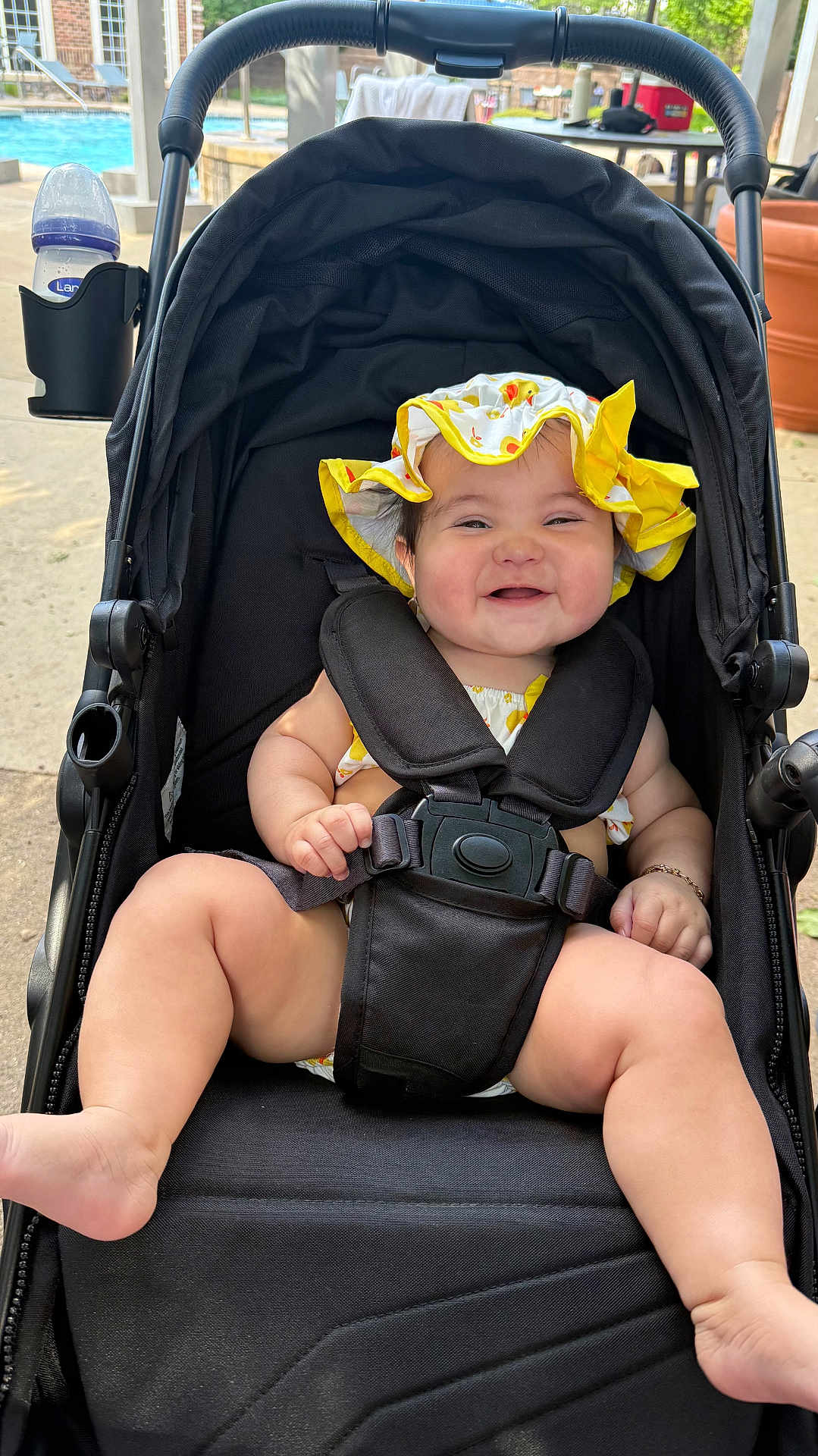 Ayla joined the competition — help win amazing prizes! baby, stroller, smiling, hat, sunhat, child, outdoor, poolside, black_stroller, happy, infant, sitting, summer, cute, baby_clothing, safety_harness, foot, hand, daylight, bracelet