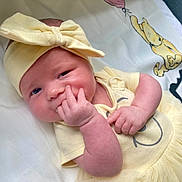 Rylee is registered to the contest to win money with this photo: baby, infant, child, yellow_clothing, headband, bow, hand, face, smiling_face, lying_down, blanket, cartoon, balloon, cute, skin, toddler, indoors, soft_texture, happy, portrait