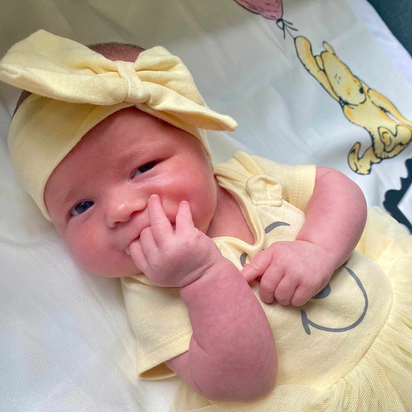 Rylee is registered to the contest to win money with this photo: baby, balloon, blanket, bow, cartoon, child, cute, face, hand, happy, headband, indoors, infant, lying_down, portrait, skin, smiling_face, soft_texture, toddler, yellow_clothing