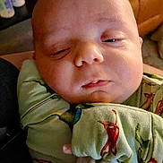 Ryker is registered to the contest to win money with this photo: baby, infant, face, sleepy, blanket, dinosaur_print, clothing, closeup, indoors, person, cute, newborn, soft_light, resting, child, portrait, hand, skin, expression, cozy