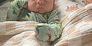 Ryker is registered to the contest to win money with this photo: baby, blanket, cushion, dinosaur_pattern, infant, indoors, person, sleepwear, soft_lighting, cute, resting, closeup, portrait, child, comfort, head, face, hand, fabric, bed