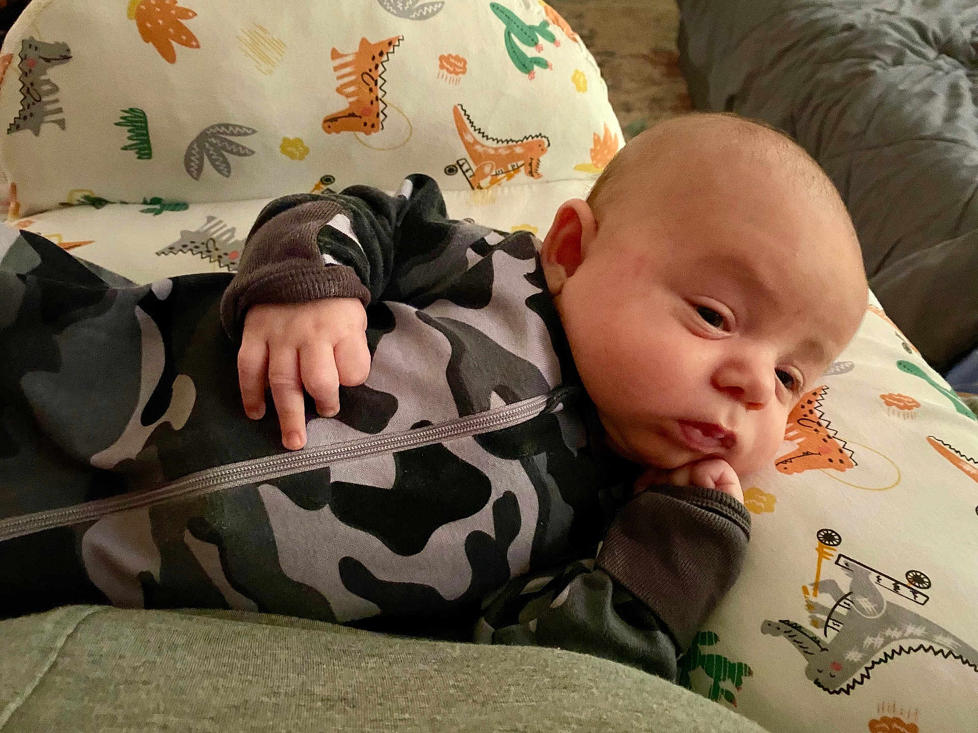 Ryker joined the competition — help win amazing prizes! baby, infant, pajamas, camo, dinosaur_pattern, pillow, hand, face, expression, thoughtful, lying_down, indoors, bedroom, child, cute, resting, closeup, skin, head, person