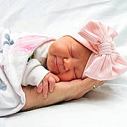 Rachel is registered to the contest to win money with this photo: newborn, baby, sleeping, pink_bow, blanket, hand, infant, soft_light, white_background, peaceful, cute, wrapped, portrait, child, headwear, smile, resting, human, closeup, tender