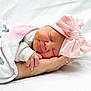 newborn, baby, sleeping, pink_bow, blanket, hand, infant, soft_light, white_background, peaceful, cute, wrapped, portrait, child, headwear, smile, resting, human, closeup, tender