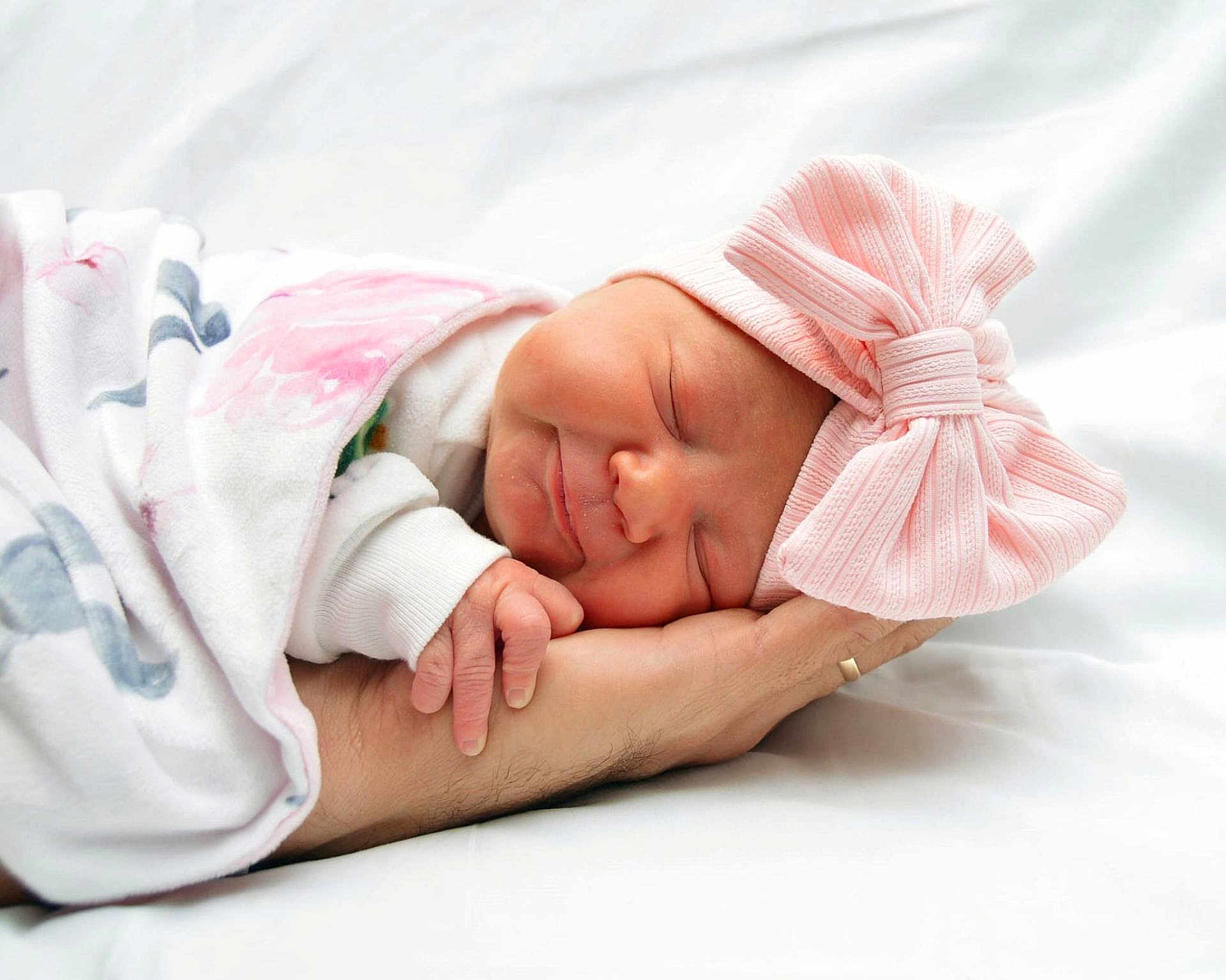 Rachel is registered to the contest to win money with this photo: newborn, baby, sleeping, pink_bow, blanket, hand, infant, soft_light, white_background, peaceful, cute, wrapped, portrait, child, headwear, smile, resting, human, closeup, tender
