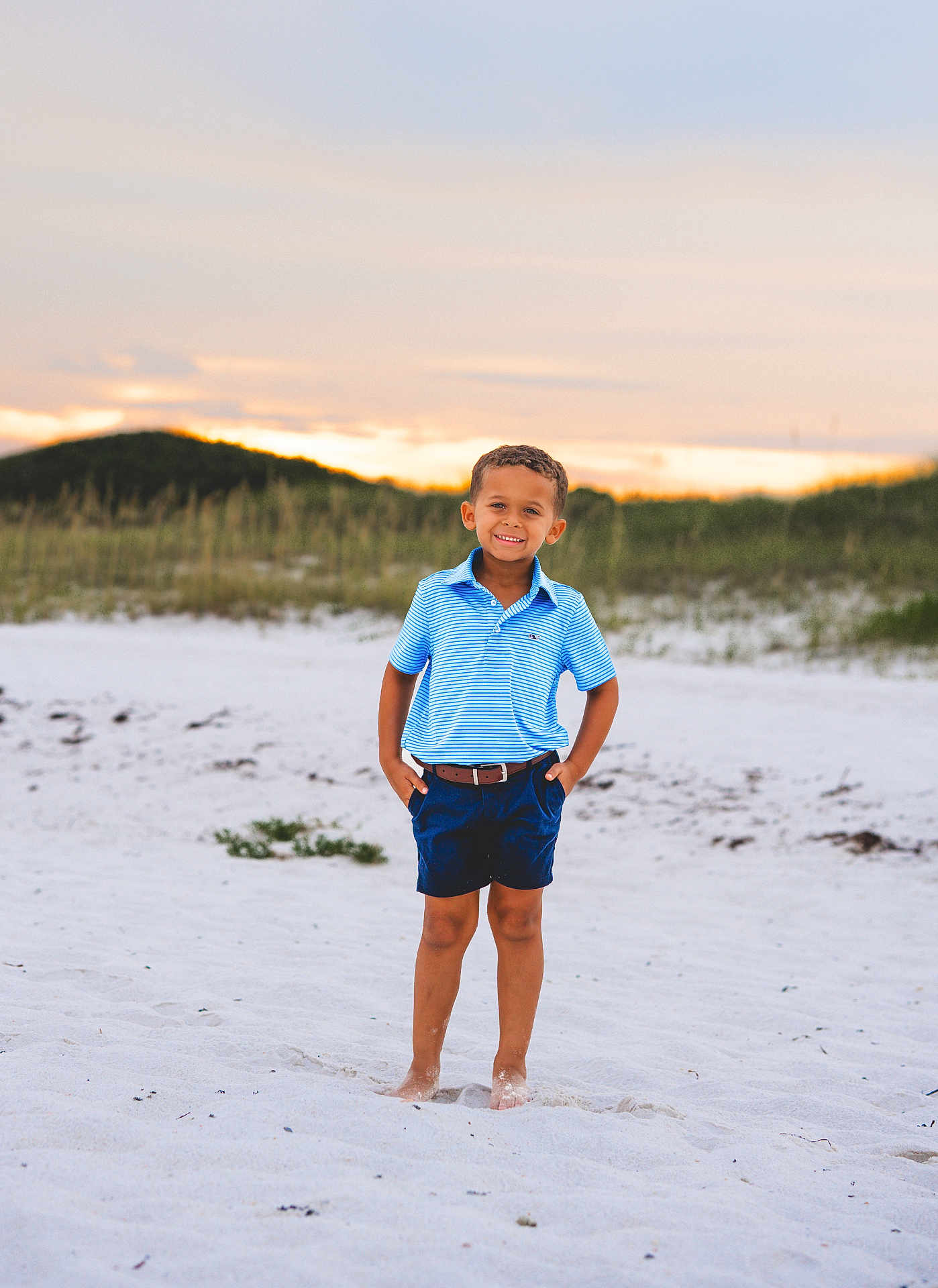 Levi joined the competition — help win amazing prizes! child, boy, beach, sand, sunset, smiling, barefoot, shorts, polo_shirt, blue_clothing, nature, outdoor, grass, dunes, sky, clouds, portrait, standing, casual, summer
