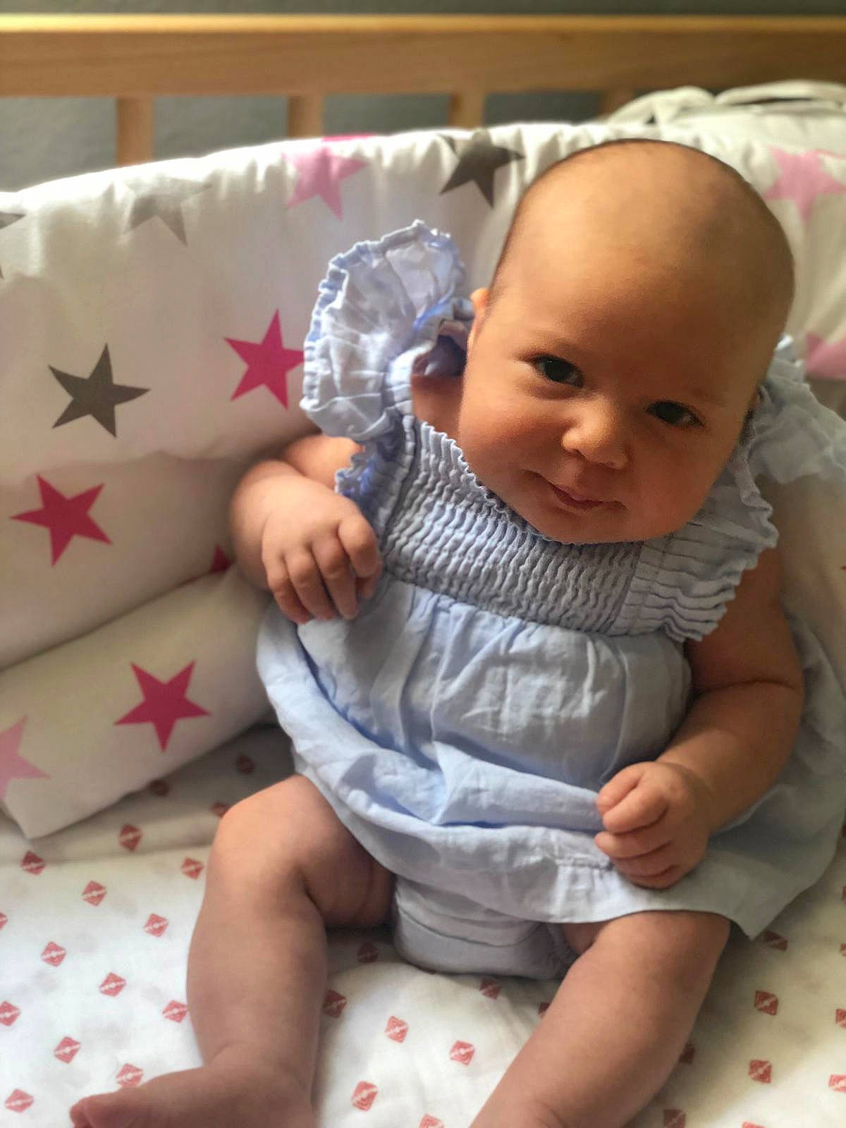 Léa participe au concours pour gagner de l'argent avec cette photo : baby, baby_toddler_clothing, cheek, child, comfort, dress, hand, human_body, lap, linens, pattern, person, product, room, sitting, skin, sleeve, smile, sock, textile