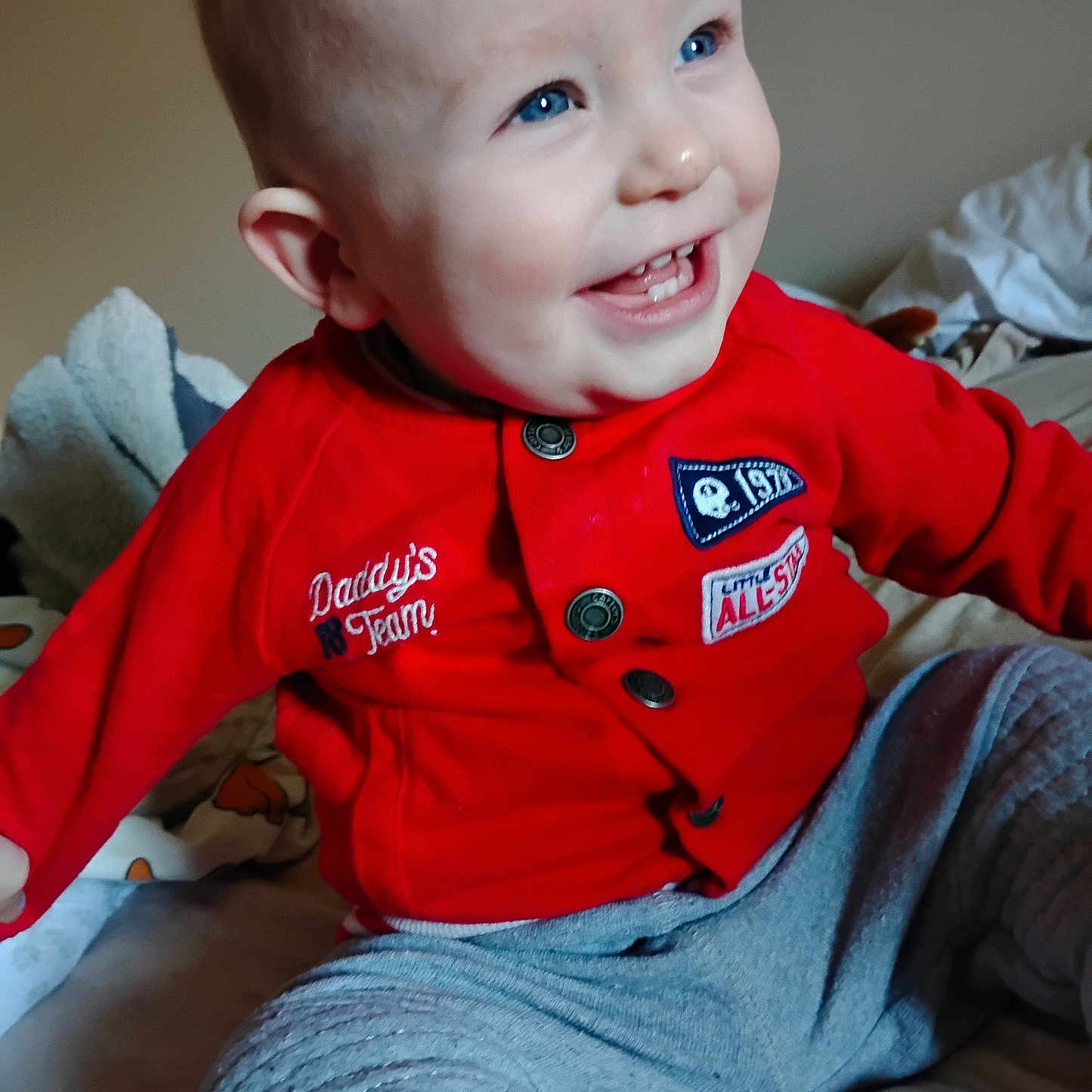 Ransom joined the competition — help win amazing prizes! baby, bed, blanket, blue_eyes, casual, child, clothing, cozy, cute, face, happy, indoor, infant, person, playful, portrait, red_jacket, sitting, smiling, young_child