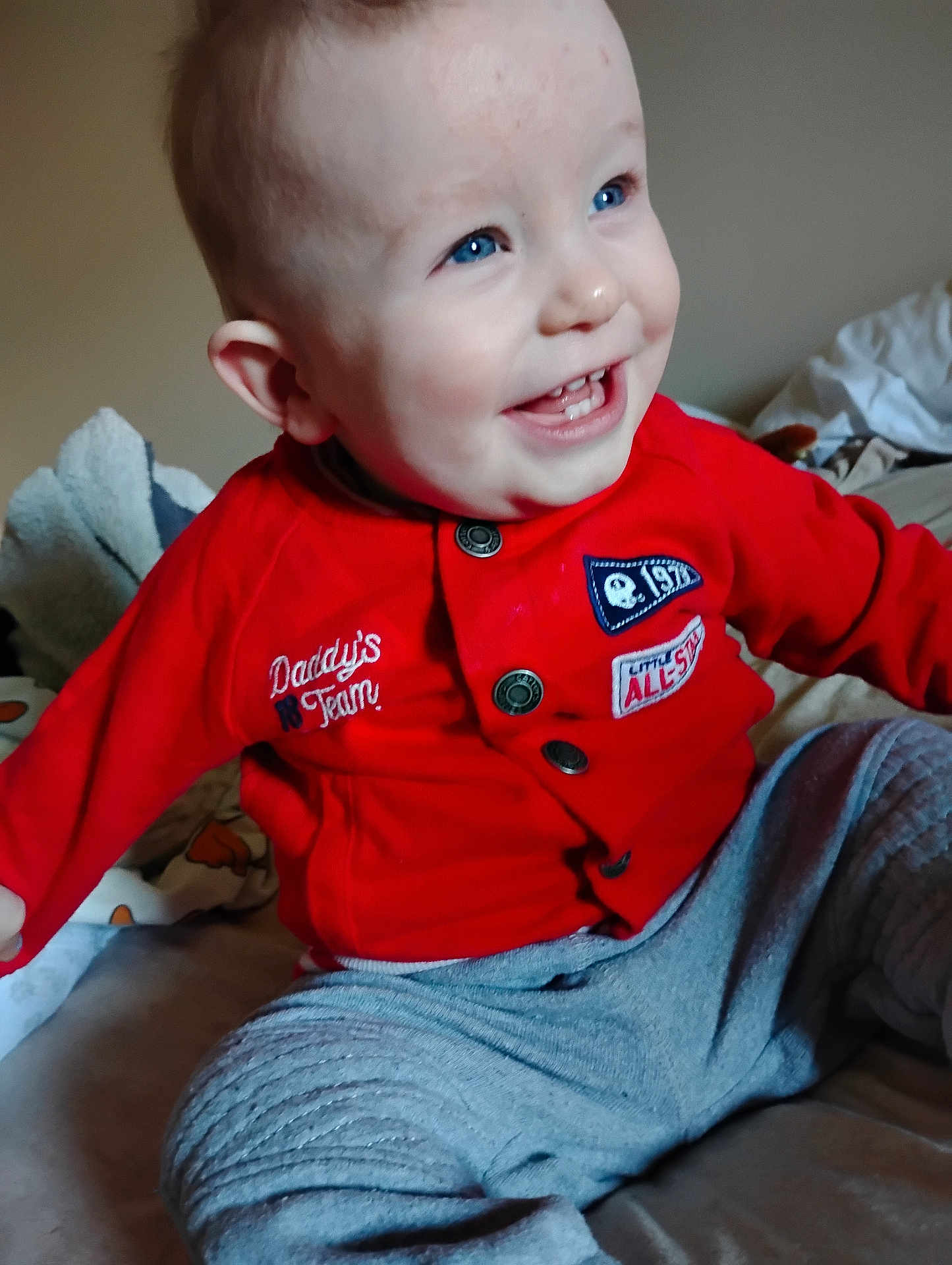 Ransom joined the competition — help win amazing prizes! baby, child, smiling, red_jacket, blue_eyes, sitting, indoor, blanket, bed, happy, cute, portrait, clothing, infant, face, person, young_child, casual, cozy, playful