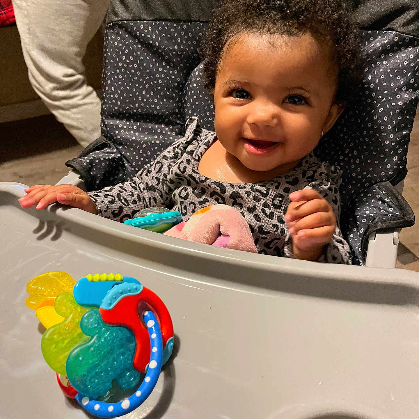 Wynterr is registered to the contest to win money with this photo: baby, high_chair, smile, toy, teething_toy, curly_hair, indoor, child, person, clothing, happy, face, seat, table, hand, cute, infant, playful, young_child, cosco_kids