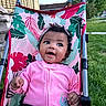 baby, child, stroller, pink_clothing, curly_hair, smiling, outdoor, grass, house, headband, toddler, portrait, happy, person, seat, daylight, nature, colorful, cute, expression
