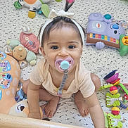 Juliana participe au concours pour gagner de l'argent avec cette photo : baby, pacifier, headband, crib, toy, stuffed_animal, floor, wood, colorful, infant, child, play, cute, smiling, sitting, indoors, clothing, expression, face, hand