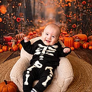 Joseph is registered to the contest to win money with this photo: baby, child, skeleton_costume, pumpkin, autumn, fall_decor, orange, smiling, cute, cozy_chair, seasonal, holiday, halloween, toddler, plush, indoor, portrait, festive, happy, costume