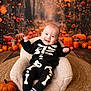 baby, child, skeleton_costume, pumpkin, autumn, fall_decor, orange, smiling, cute, cozy_chair, seasonal, holiday, halloween, toddler, plush, indoor, portrait, festive, happy, costume