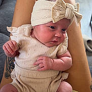 Remi is registered to the contest to win money with this photo: baby, infant, headband, bow, clothing, socks, tattoo, legs, person, indoor, couch, floor, curious, skin, pattern, fabric, comfortable, seated, portrait, home