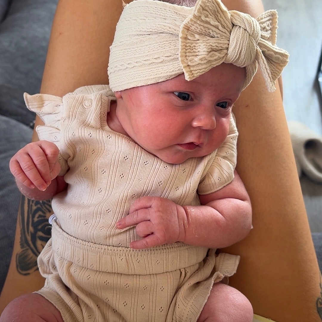 Remi is registered to the contest to win money with this photo: baby, bow, clothing, comfortable, couch, curious, fabric, floor, headband, home, indoor, infant, legs, pattern, person, portrait, seated, skin, socks, tattoo