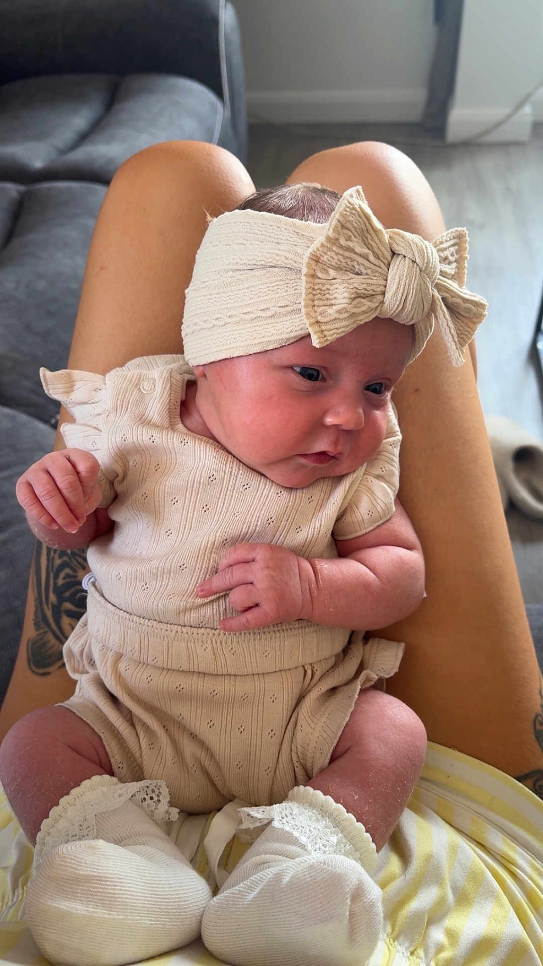 Remi is registered to the contest to win money with this photo: baby, infant, headband, bow, clothing, socks, tattoo, legs, person, indoor, couch, floor, curious, skin, pattern, fabric, comfortable, seated, portrait, home