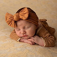Iris a rejoint le concours — aidez-le/la à gagner de superbes lots ! baby, sleeping, headband, bow, knitted_clothing, brown, beige, blanket, soft_texture, newborn, peaceful, portrait, cute, infant, resting, closeup, hands, face, cozy, warm_colors